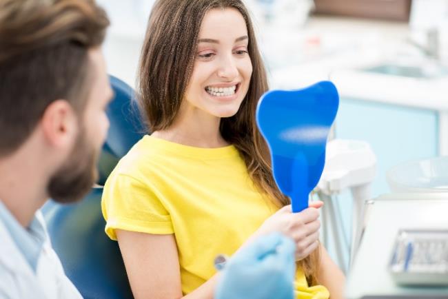 אישה בוחנת את השיניים מול מראה לאחר טיפול שיניים מותאם אישית